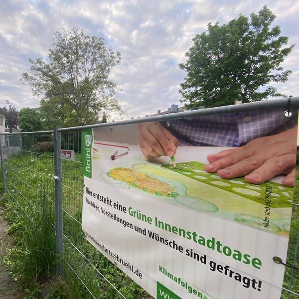 Zu sehen ist ein Bauzaun, an dem ein Banner angebracht ist, das auf die geplante Innenstadtoase hinweist.