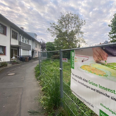 Zu sehen ist ein Bauzaun, an dem ein Banner angebracht ist, das auf die geplante Innenstadtoase hinweist.