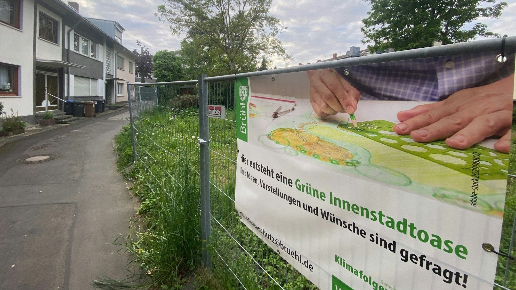 Zu sehen ist ein Bauzaun, an dem ein Banner angebracht ist, das auf die geplante Innenstadtoase hinweist.