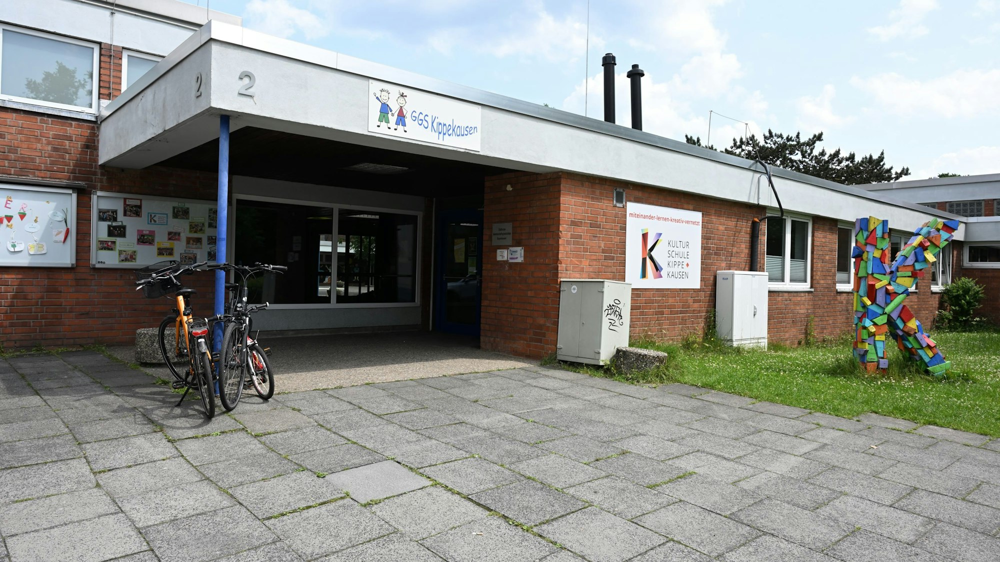 Der Eingang zum Schulgebäude ist zu sehen, davor stehen zwei Fahrräder.