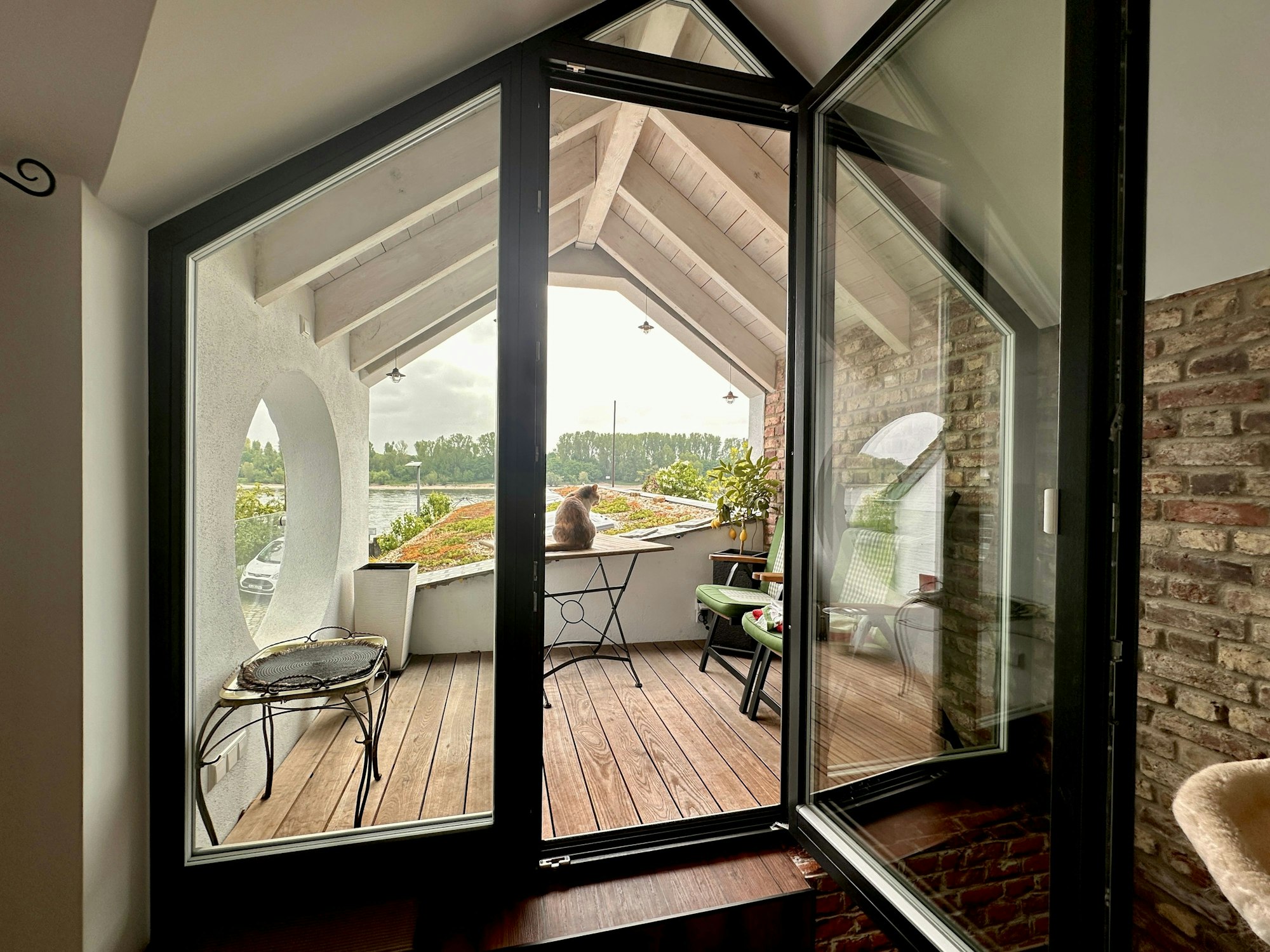 Auf einer Loggia stehen ein Tisch und Stühle, dahinter ist der Rhein zu sehen.