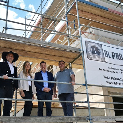 Auf dem Gerüst eines Neubaus stehen Markus Wellens, Leoni Vogel, Bürgermeister Sacha Reichelt und Projektleiter Roman Engel nebeneinander und schauen herab.