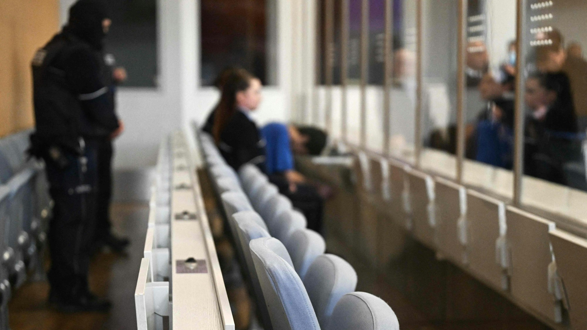 Im Gerichtssaal: Die Anklagebank mit einem Mann und einer Frau im Hintergrund ist zu sehen.