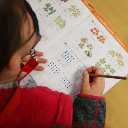 Eine Schülerin schreibt im Unterricht in ihr Schulbuch.