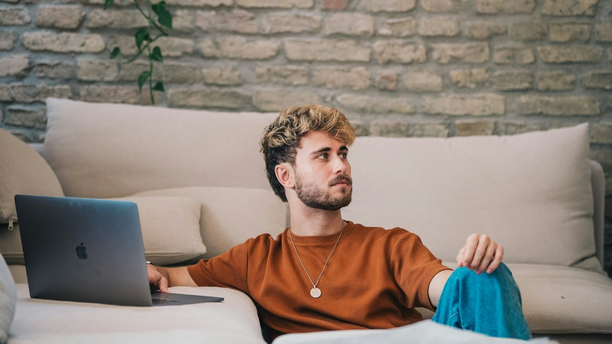 Ein junger Mann sitzt an einer Couch-Landschaft vor seinem Laptop.