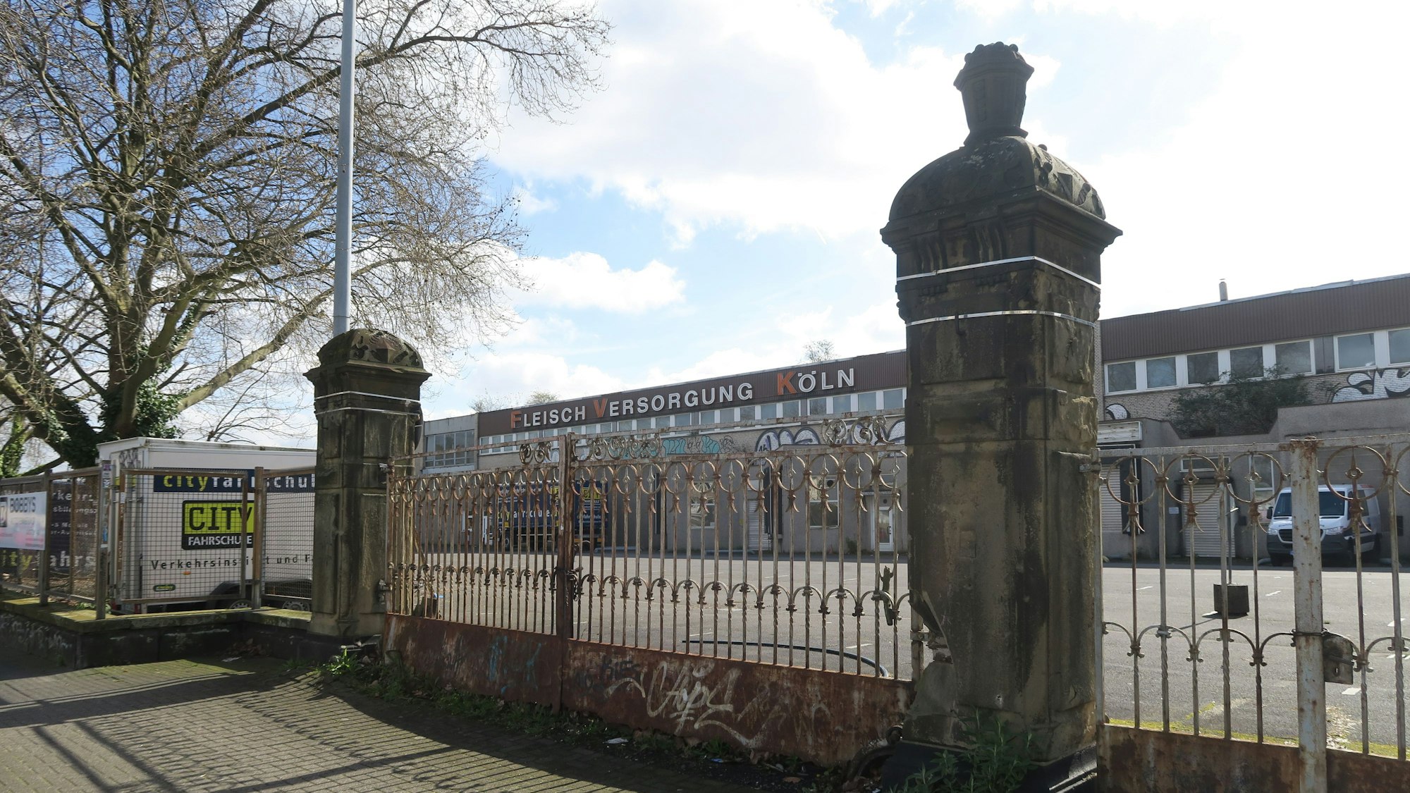Ein großes Tor mit weitläufigen Hallen dahinter ist zu sehen. Es handelt sich um das ehemalige Gelände des Kölner Schlachthofs.