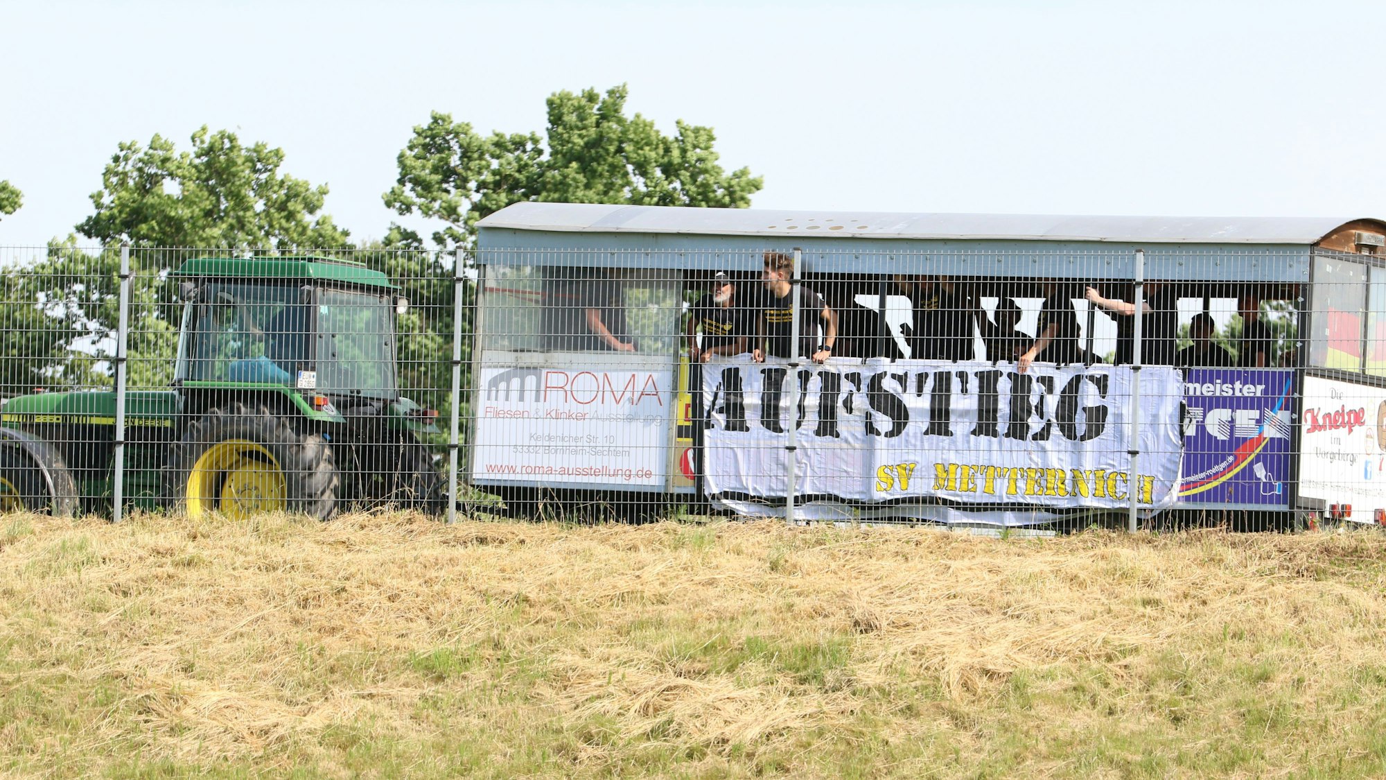 Ein Traktor fährt am Sportplatz von Lommersum vorbei, auf dem Anhänger die Spieler des SV Metternich, die ihren Aufstieg feiern.