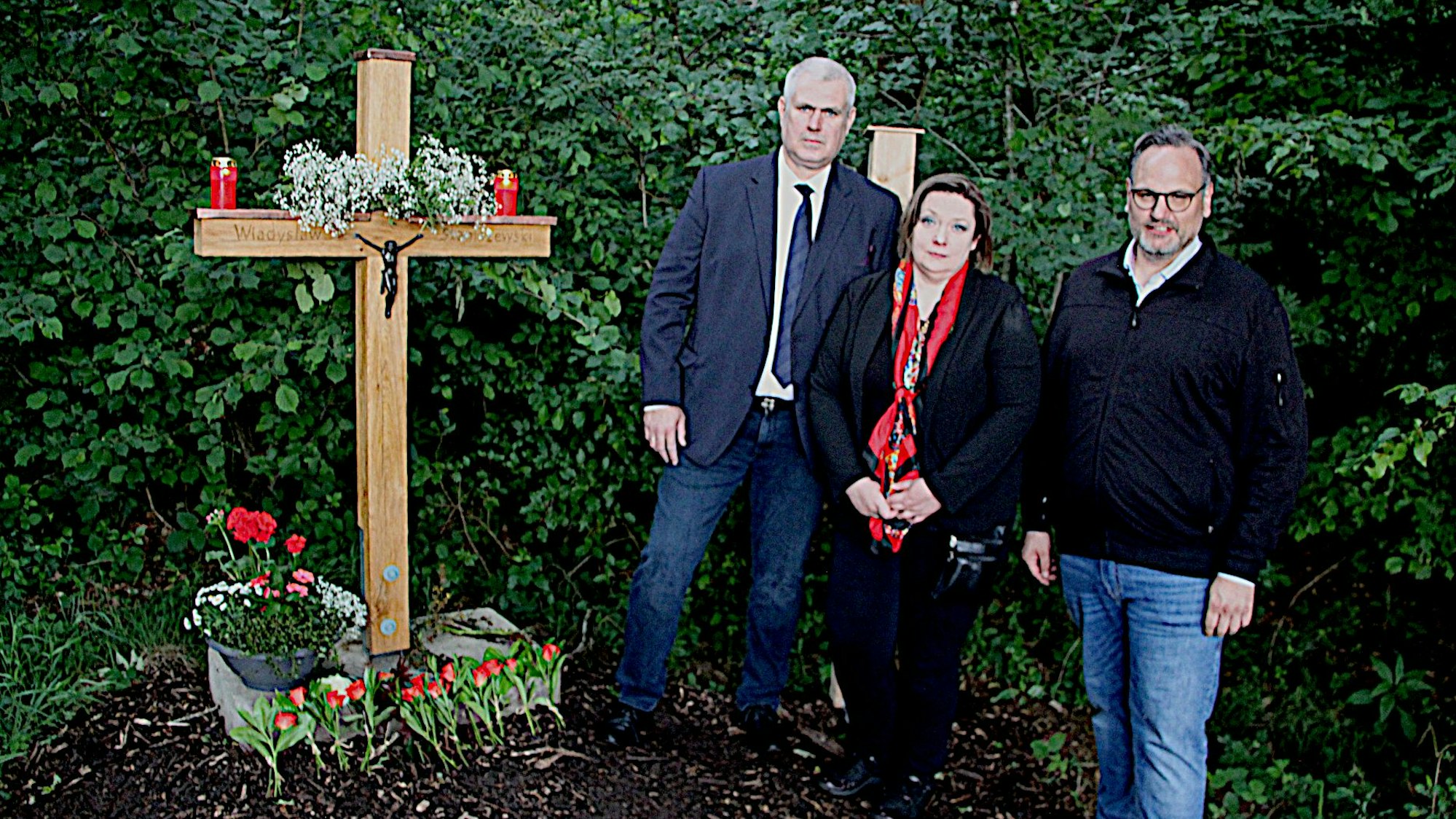 Aneta und Pjotr Jagans sowie Jochen Kirwel stehen neben dem Gedenkkreuz.