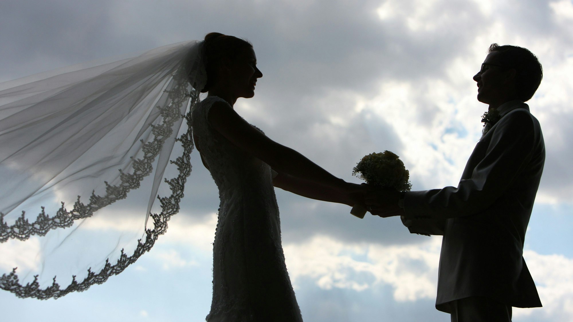 Die Silhouette eines frisch vermählten Hochzeitspaares zeichnet sich im Gegenlicht ab.