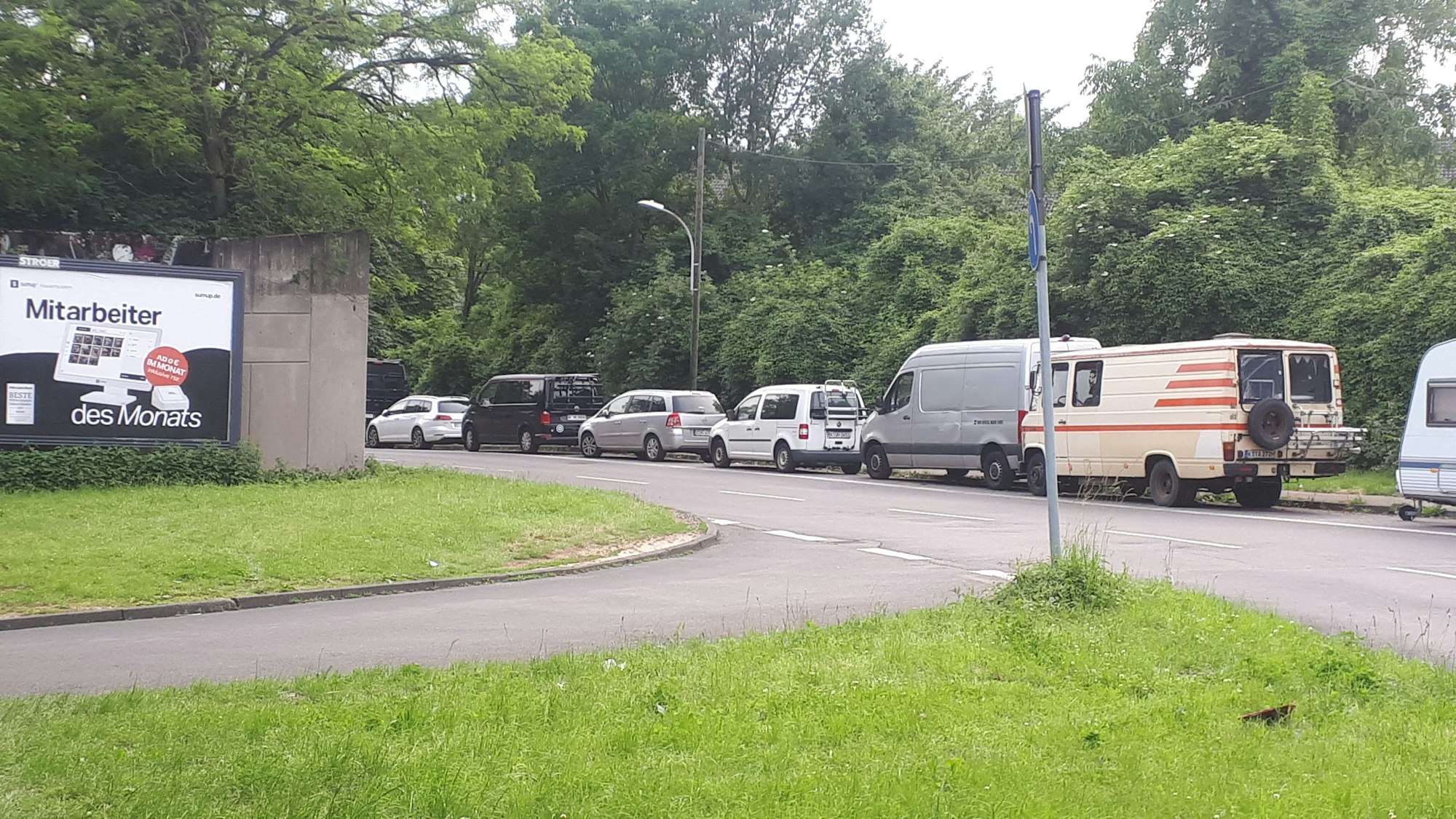An einer zweispurigen Straße parken viele Autos und auch Vans.