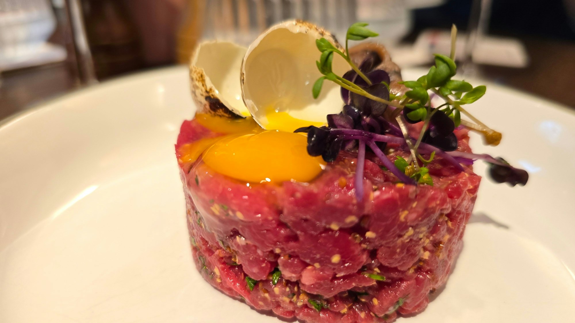 Das Tatar liegt als geformter Zylinder auf dem Teller, obendrauf ein Eigelb und etwas Sprossendeko.