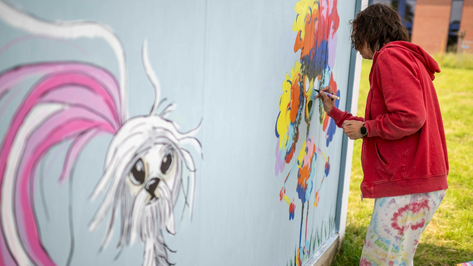 Das Bild zeigt eine Künstlerin, die einen Container mit bunten Hunden bemalt.