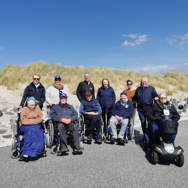 Fünf Menschen im Rollstuhl sowie Pflegende und Angehörige auf Norderney vor den Dünen.