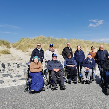 Fünf Menschen im Rollstuhl sowie Pflegende und Angehörige auf Norderney vor den Dünen.