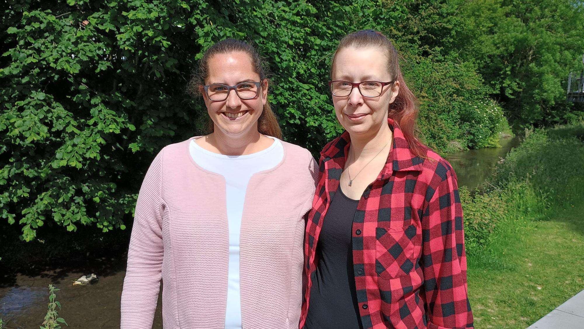 Die beiden stehen beieinander und lächeln. Hinter ihnen fließt die Kleine Erft, am Ufer dichtes Blattwerk der Bäume.