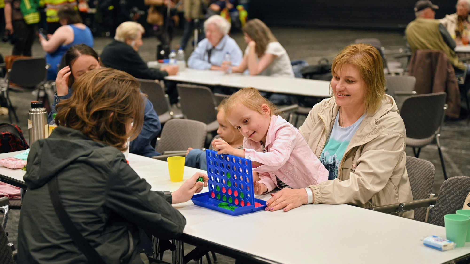 04.06.2025, Nordrhein-Westfalen, Köln: Eine Familie vertreibt sich die Zeit in der Anlaufstelle der Stadt Köln mit spielen. Am Montag waren im Stadtteil Deutz drei Bomben aus dem Zweiten Weltkrieg entdeckt worden. Foto: Henning Kaiser/dpa - ACHTUNG: Nur zur redaktionellen Verwendung im Zusammenhang mit der aktuellen Berichterstattung über die Bombenentschärfung und nur mit vollständiger Nennung des vorstehenden Credits +++ dpa-Bildfunk +++