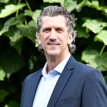 Auf dem Bild ist ein Portrait des Niederlassungsleiter der Deutschen Marktgilde zu sehen, er trägt einen dunklen Anzug und eine Krawatte.