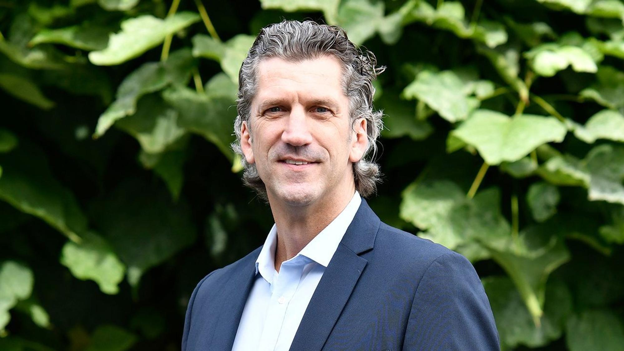 Auf dem Bild ist ein Portrait des Niederlassungsleiter der Deutschen Marktgilde zu sehen, er trägt einen dunklen Anzug und eine Krawatte.