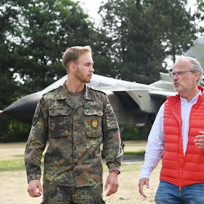 Die beiden Männer sind im Gespräch unterwegs auf dem Kasernengelände. Der junge trägt Uniform in Tarnfarbe.