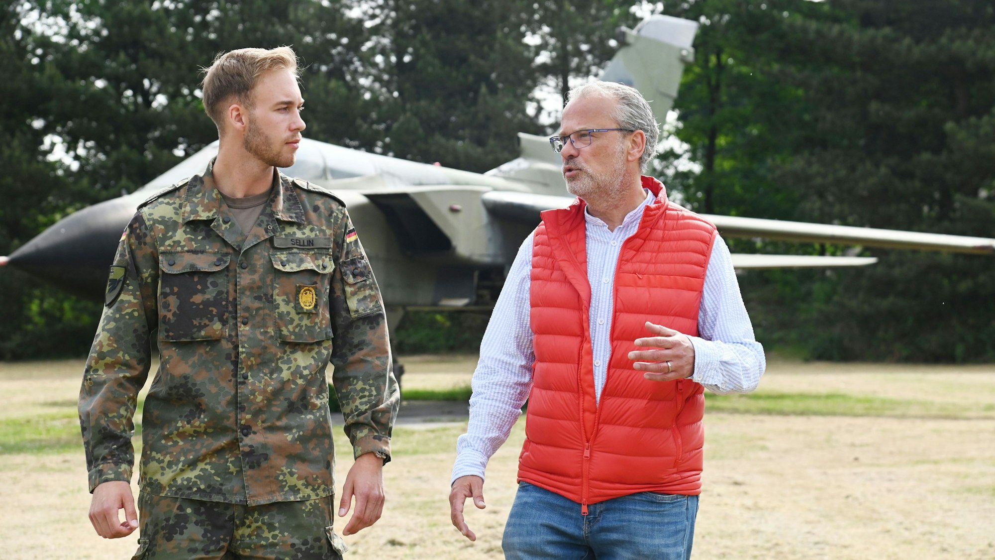 Die beiden Männer sind im Gespräch unterwegs auf dem Kasernengelände. Der junge trägt Uniform in Tarnfarbe.