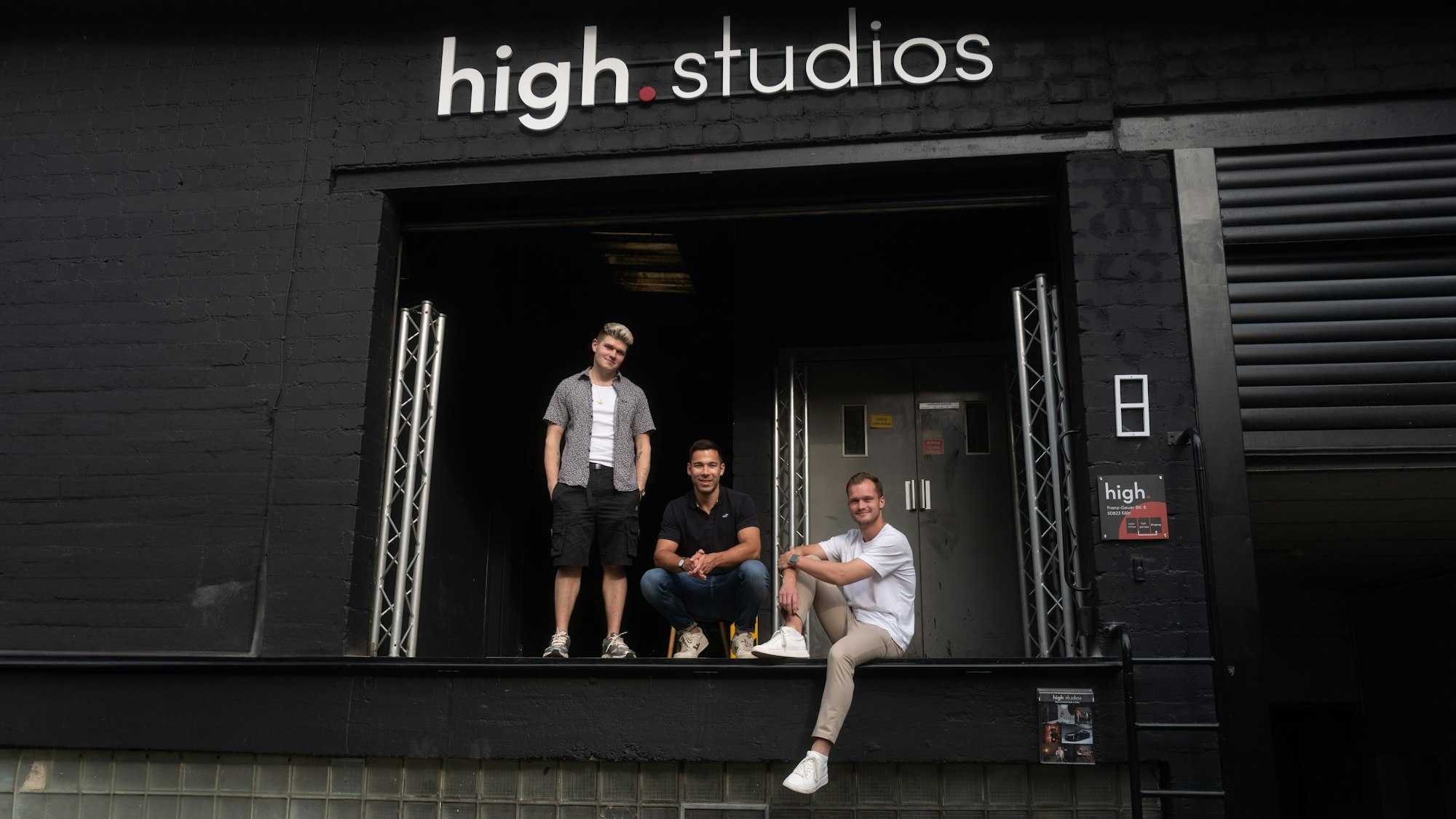 Drei Männer stehen vor einem Studio-Eingang. Das Studio heißt high.studios