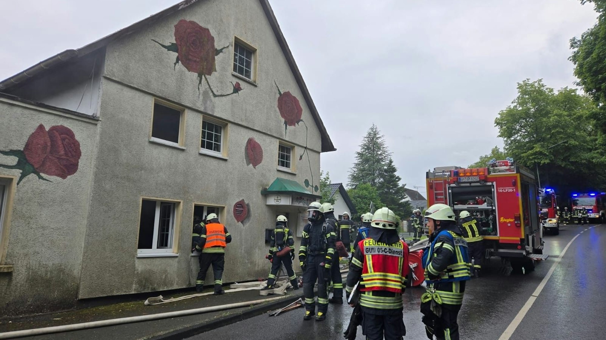 Einsatzkräfte der Feuerwehr stehen vor dem Gebäude.