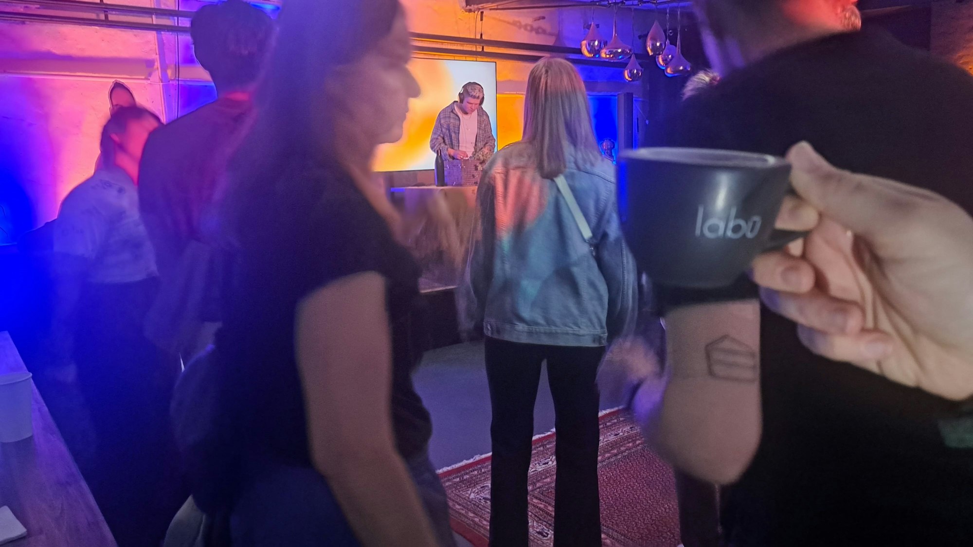 Menschen tanzen bei einer Party in einem Studio. Eine Kaffeetasse wird ins Bild gehalten.