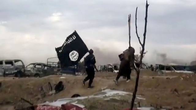 ARCHIV - 19.03.2019, Syrien, Baghus: IS-Kämpfer laufen mit einer IS-Flagge. (Screenshot aus einem Video der Amaq News Agency, dem Medienarm des Islamischen Staates - Beste verfügbare Qualität; Illustration zu "14-jähriger Kölner unter Terrorverdacht") Foto: Amaq News Agency/AP/dpa +++ dpa-Bildfunk +++