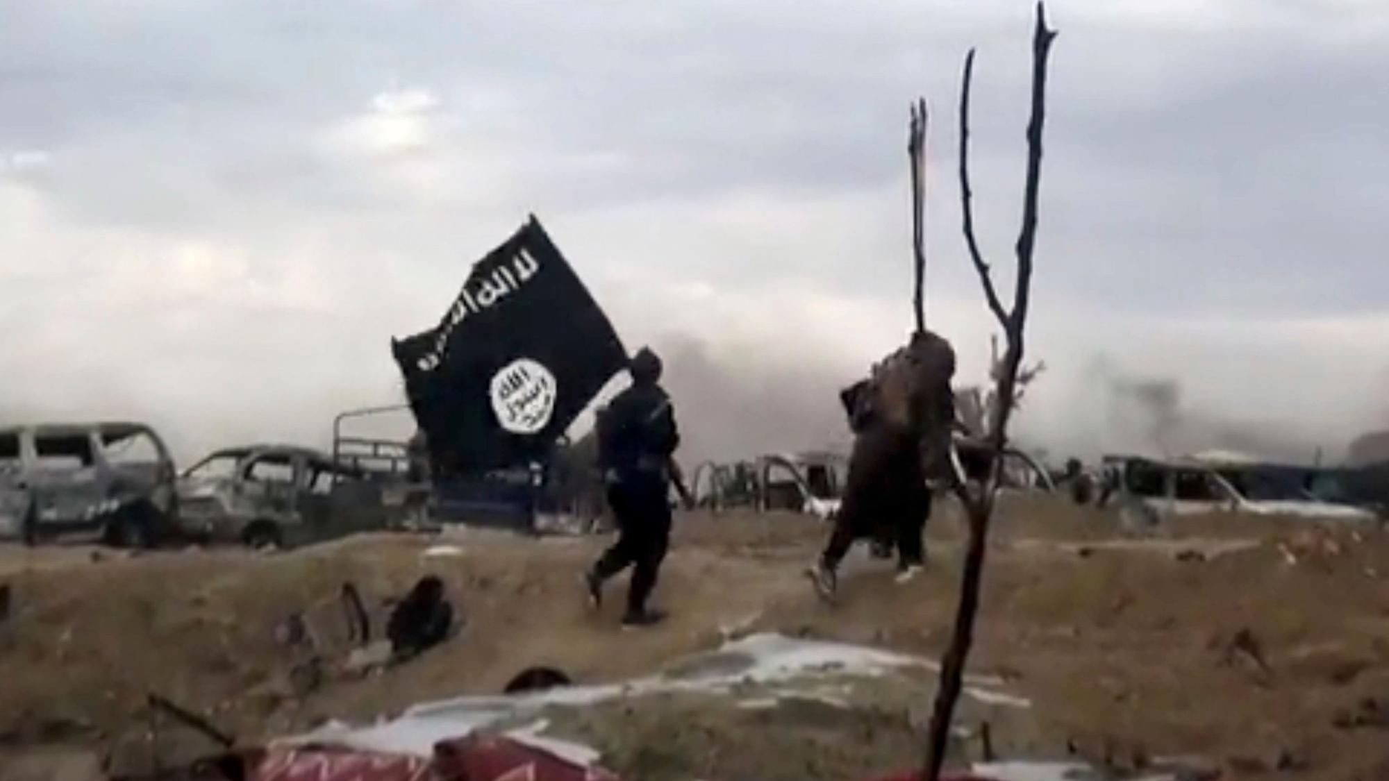ARCHIV - 19.03.2019, Syrien, Baghus: IS-Kämpfer laufen mit einer IS-Flagge. (Screenshot aus einem Video der Amaq News Agency, dem Medienarm des Islamischen Staates - Beste verfügbare Qualität; Illustration zu "14-jähriger Kölner unter Terrorverdacht") Foto: Amaq News Agency/AP/dpa +++ dpa-Bildfunk +++