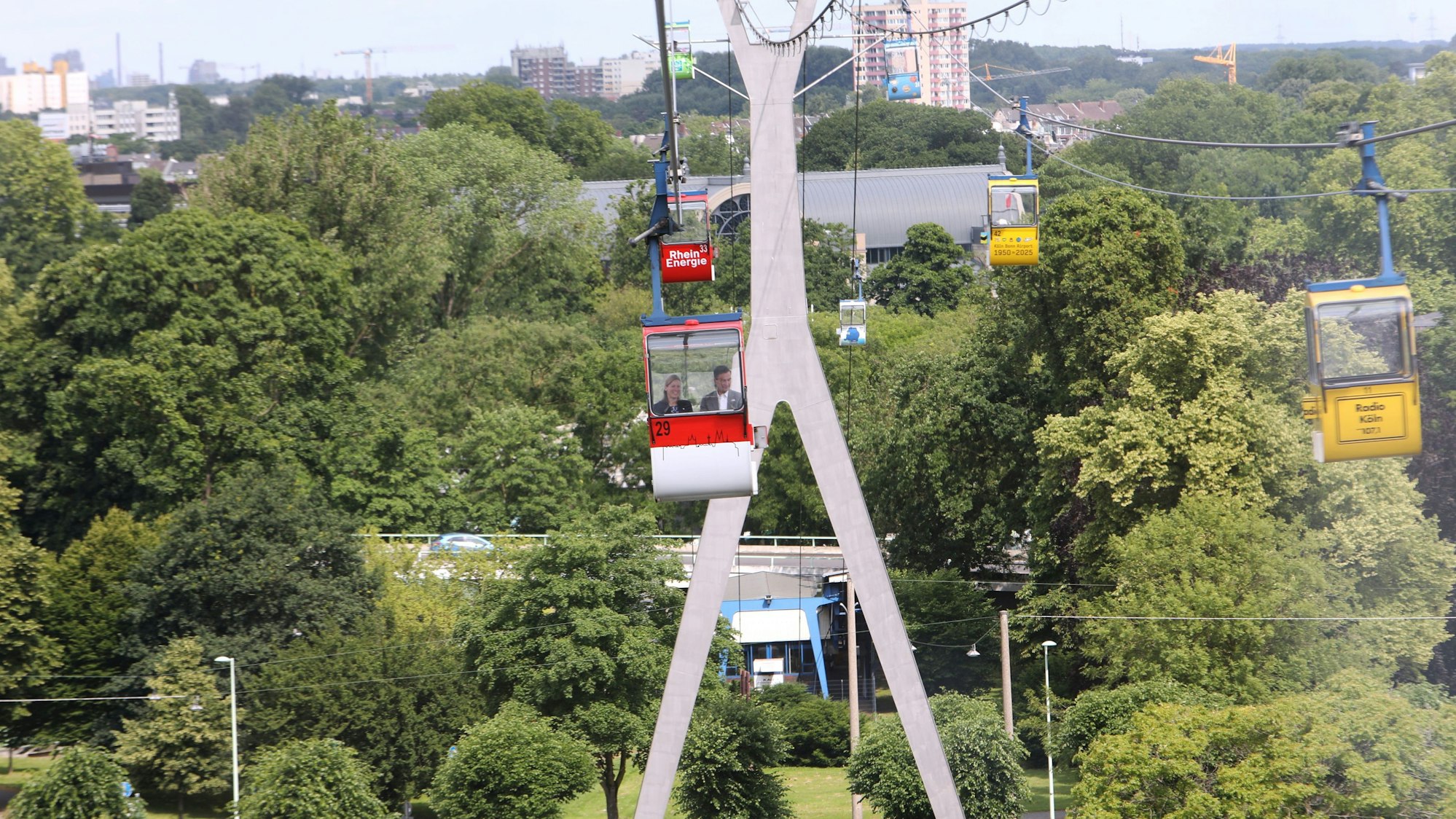Zu sehen sind Seilbahnen über Kölner Grünflächen.