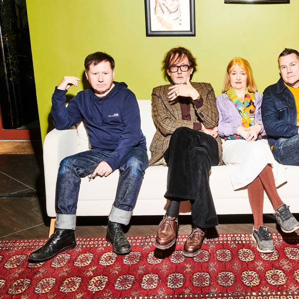 Die vier verbliebenen Mitglieder von Pulp sitzen auf einem weißen Sofa vor hellgrüner Wand.