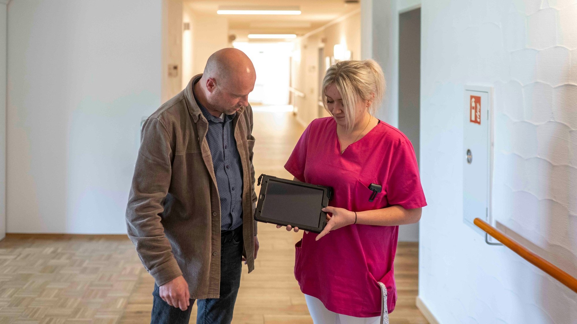 Heimleiter Lars Hammer und Melanie Klein stehen auf einem Flur im Kreuser-Stift und schauen auf ein Tablet, das Klein in den Händen hält.