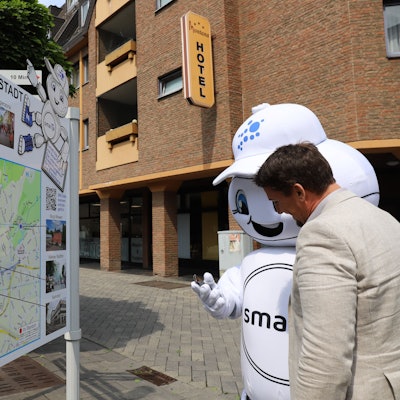 Smart City-Maskottchen SmarTa erklärt Bürgermeister Alexander Biber die App für die Entdeckungstouren.