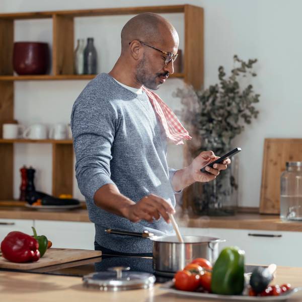 Ein Mann, der in der Küche einen Topf umrührt und sein Smartphone benutzt.