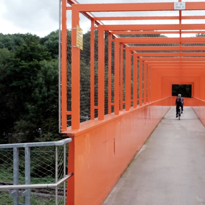 Ein Radfahrer fährt über eine orangefarbene Stahlbrücke.
