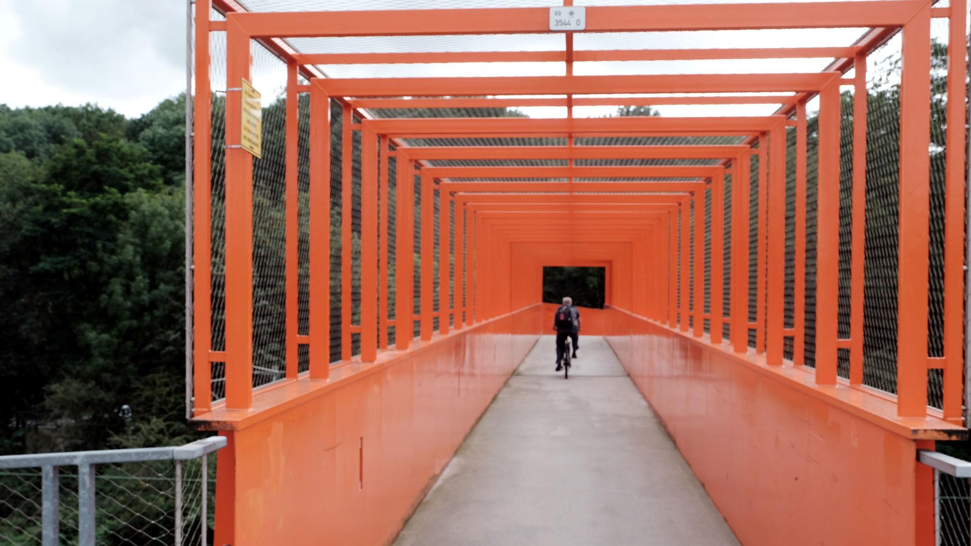 Ein Radfahrer fährt über eine orangefarbene Stahlbrücke.