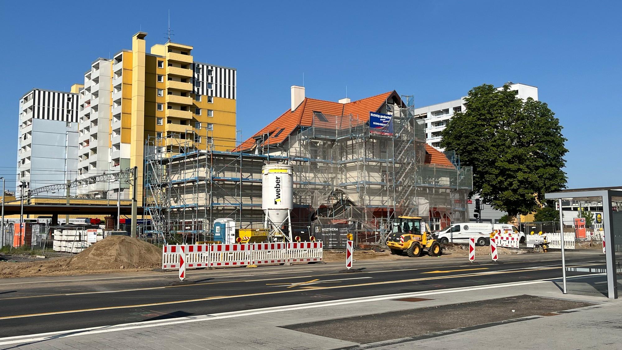 Das Bild zeigt den Bürgerbahnhof von Gerüsten umgeben, davor das bunte Treiben der Baustelle mit Verkehrsbarrieren und Fahrzeugen.