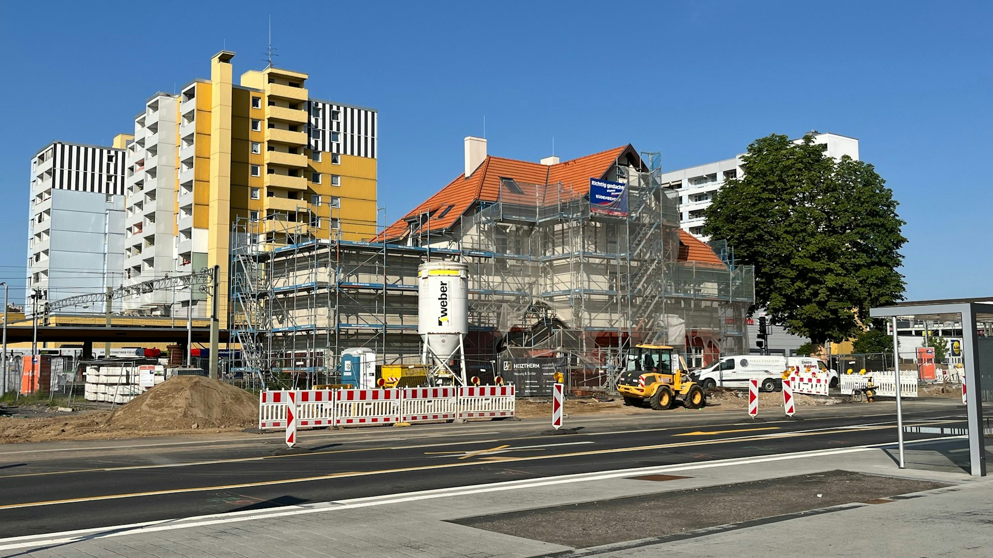 Das Bild zeigt den Bürgerbahnhof von Gerüsten umgeben, davor das bunte Treiben der Baustelle mit Verkehrsbarrieren und Fahrzeugen.