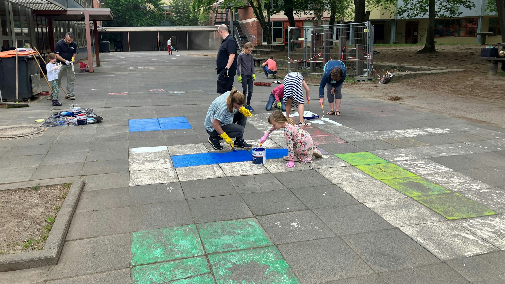 Kinder und Erwachsene malen mit Pinsel neue Markierungen auf den Boden.