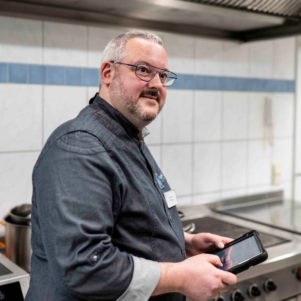 Küchenchef Timo Caspers steht in der Küche und hat ein Tablet in der Hand.