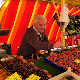 Ein Mann bedient einen Kunden auf einem Wochenmarkt, der gerade Erdbeeren gekauft hat.