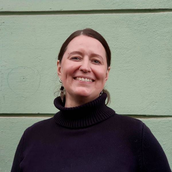 Eine Frau mit dunklem Pullover und dunklem Haar lächelt in die Kamera.