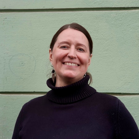 Eine Frau mit dunklem Pullover und dunklem Haar lächelt in die Kamera.