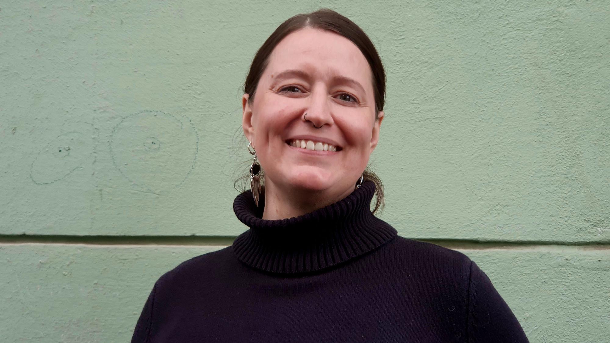 Eine Frau mit dunklem Pullover und dunklem Haar lächelt in die Kamera.