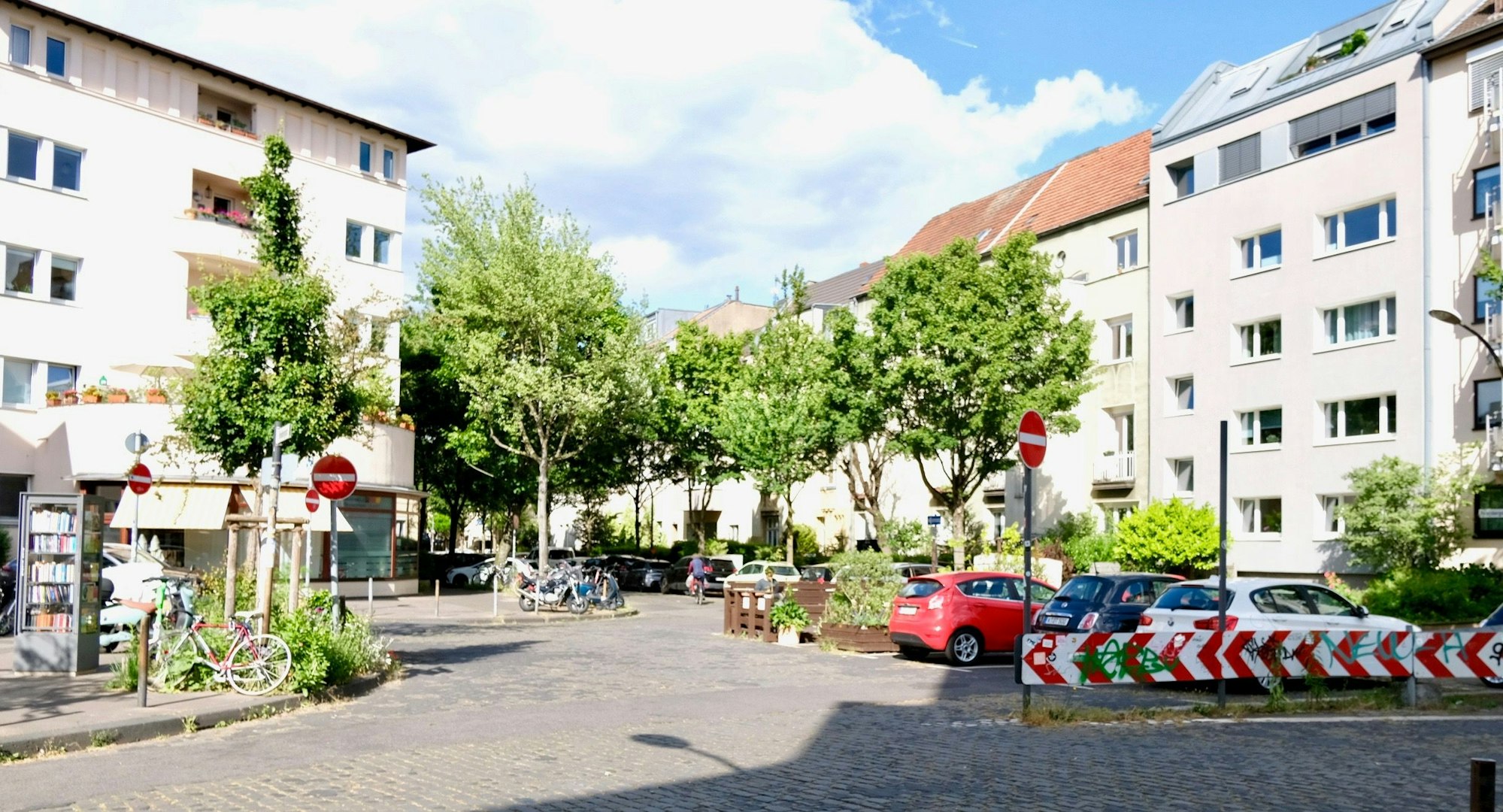 Neben parkenden Autos stehen Holzmöbel, ein sogenanntes Parklet, und Pflanzen.