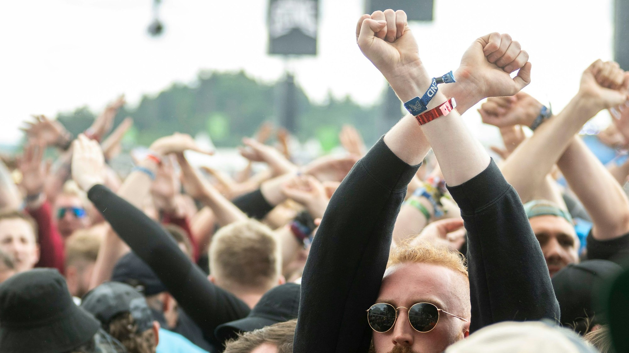 Das Bild zeigt Fans, die die Handgelenke über dem Kopf verschränken.