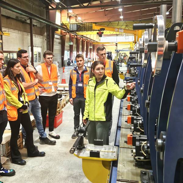 Eine Gruppe Menschen steht in Warnwesten gekleidet in einer Produktionshalle.