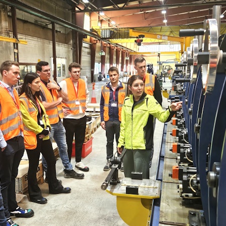 Eine Gruppe Menschen steht in Warnwesten gekleidet in einer Produktionshalle.