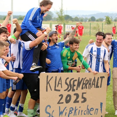 Die Wißkirchener Spieler stehen hinter einer Pappe, auf der "Klassenerhalt 2025" steht. Ihren Trainer Horst Bartz tragen sie auf Schultern.
