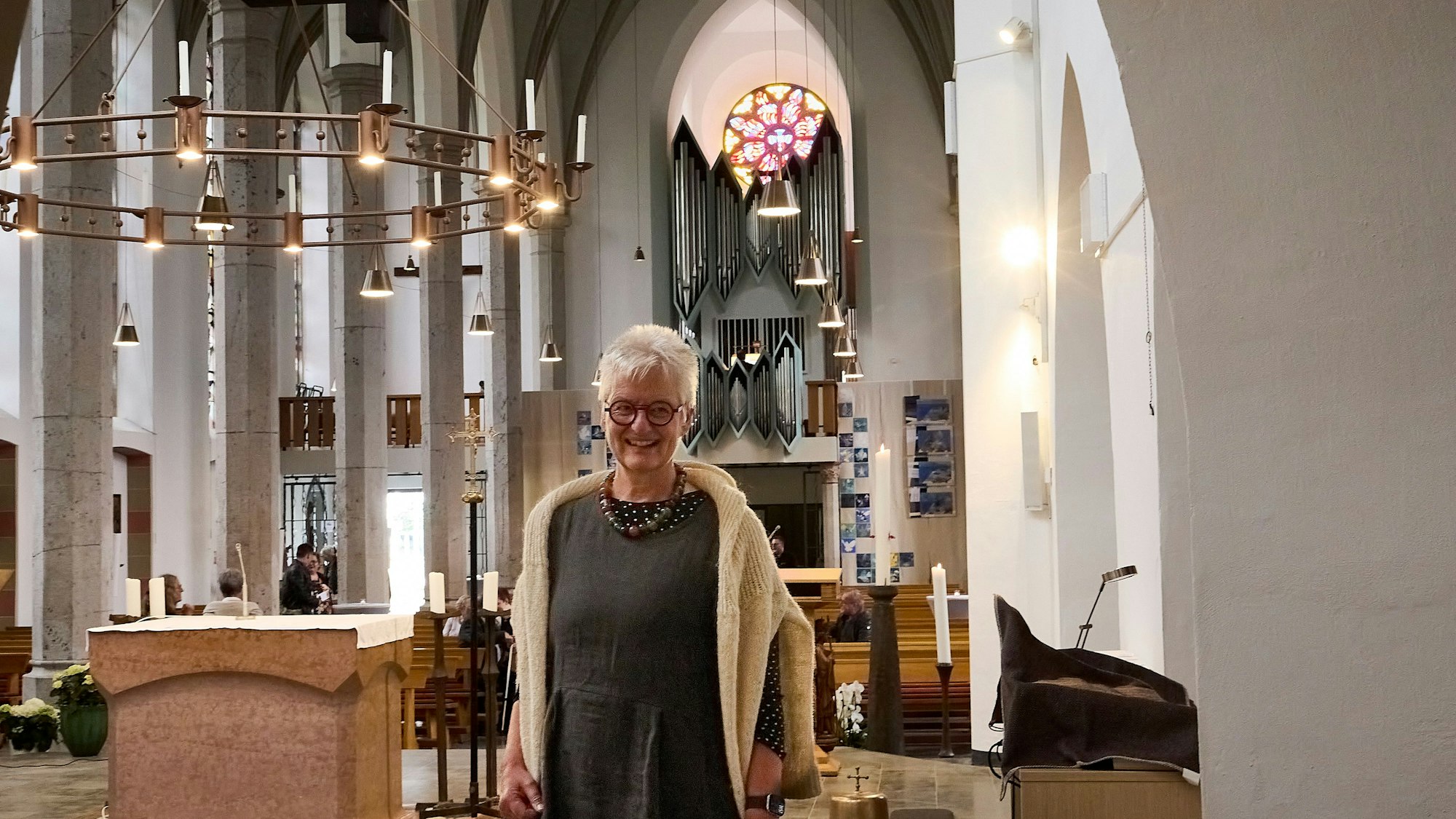 Jutta Höfs steht in der Gemünder Kirche, hinter ihr sind die Bänke, die Orgel und ein rundes, buntes Fenster zu sehen.